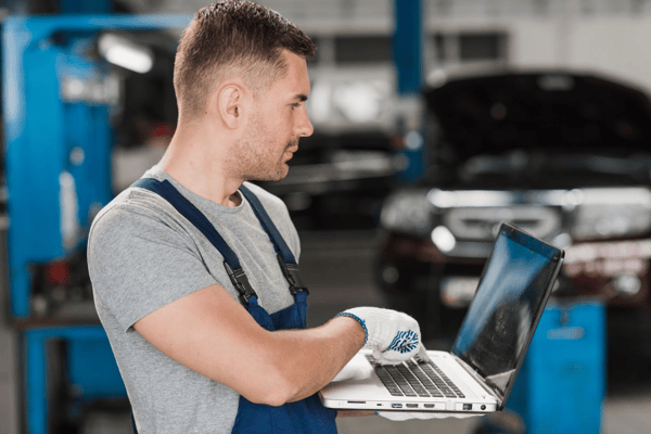 Técnico automotor revisando datos logísticos en laptop dentro de taller de mantenimiento